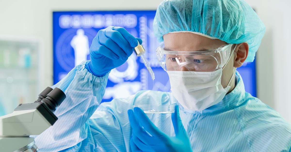 研究室で顕微鏡を使う無菌衣を着用した男性研究者