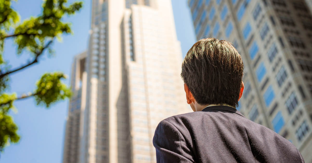 Man gazing upwards at the top of a tall company building