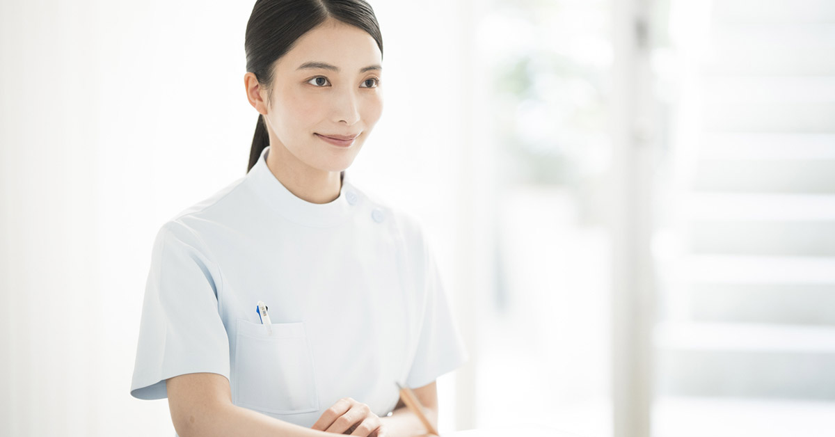 明るい室内でデスクに座り、書類に記入している看護師の女性