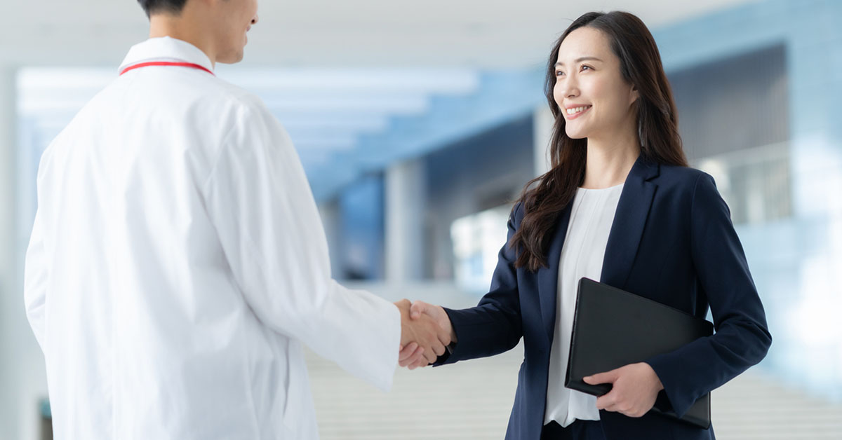 医師と握手するスーツ姿の女性MSLがキャリアアップや専門性を示すビジネスシーンのイメージ
