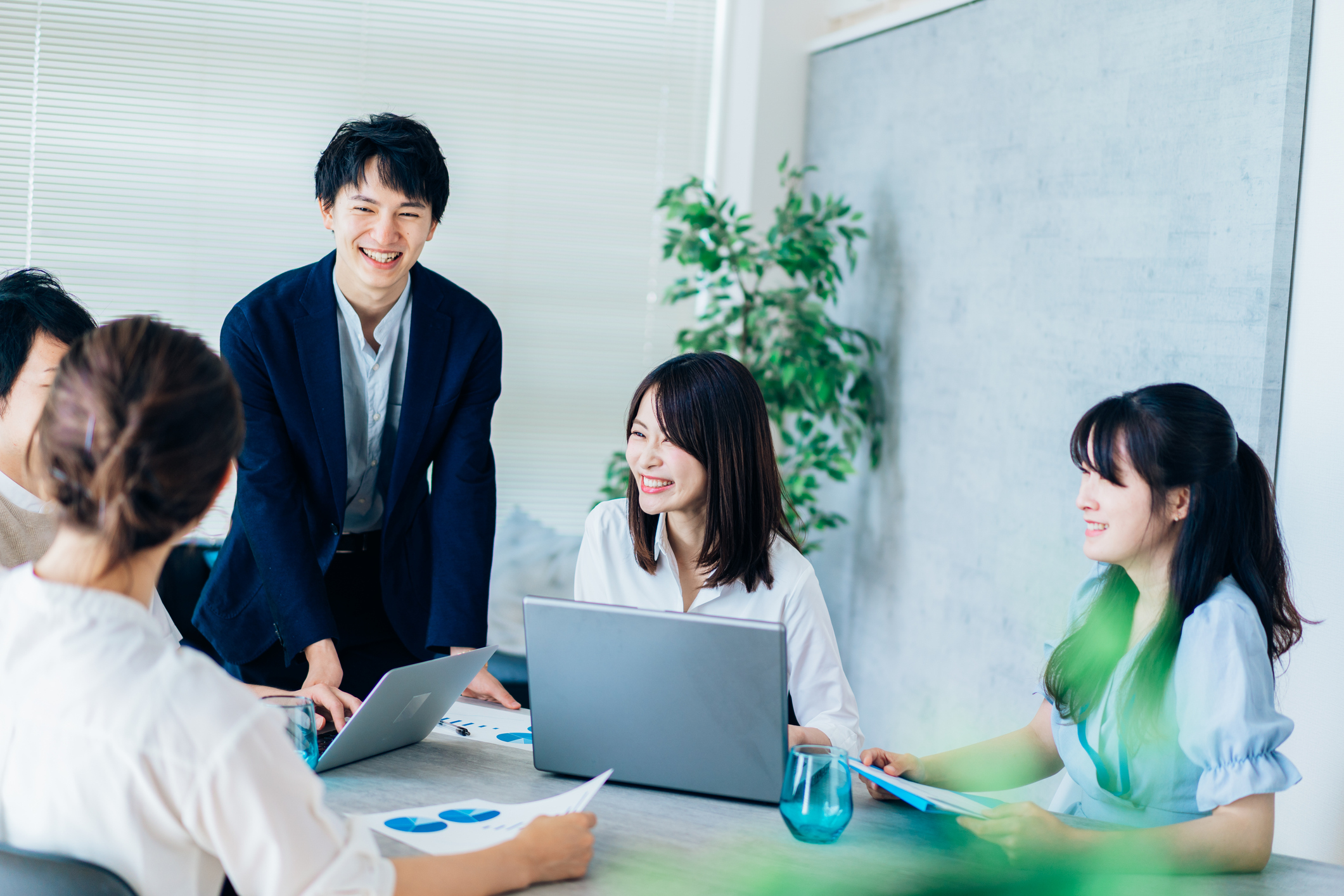 スタートアップ企業のオフィスで男女メンバーが会議テーブルを囲み、資料を確認しながら楽しそうに話し合う様子