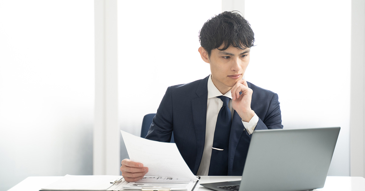 自己PRが書けなくて悩む男性が、ノートPCの前で自己分析の棚卸しをし、求人票を見ながら求められる人物像を整理しているシーン