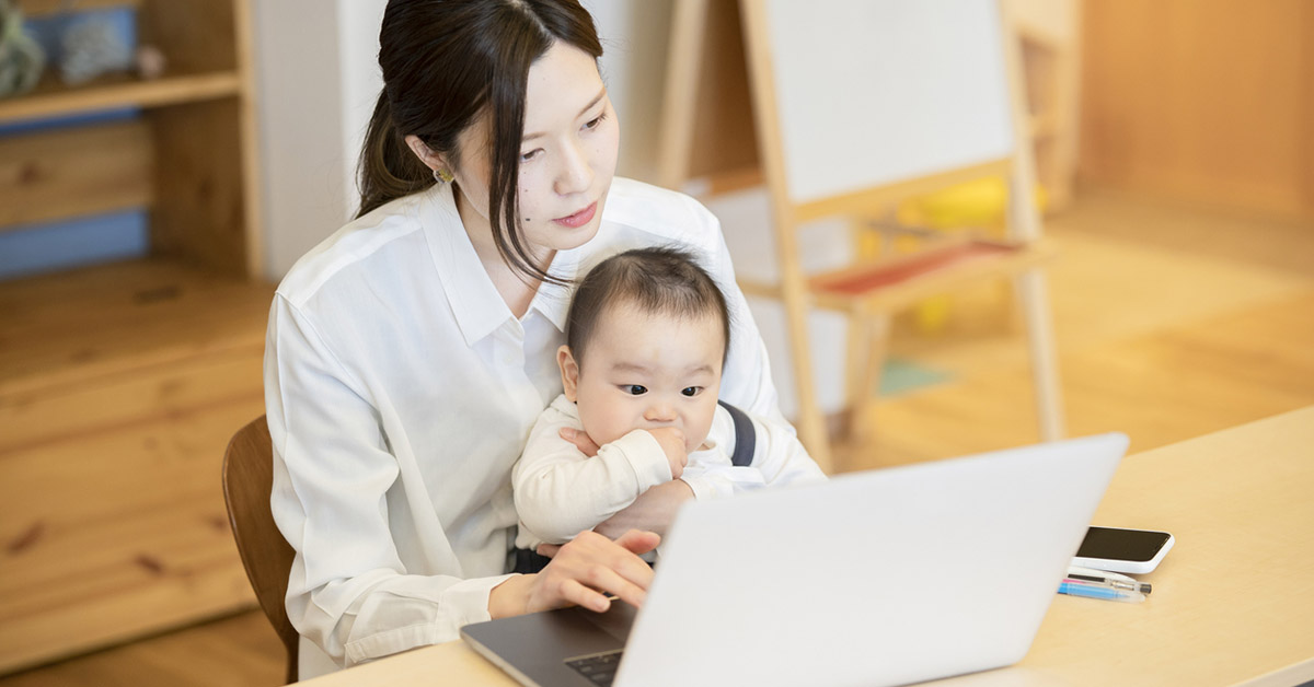IT業界のホワイト企業で働く女性が、自宅で子どもを膝にのせながら在宅勤務をしている様子