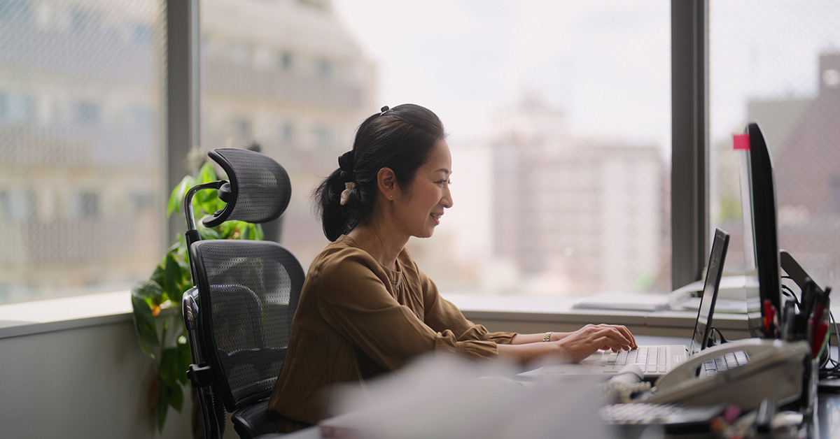 大きな窓の前でパソコンを使い、履歴書テンプレートに経験やスキルを丁寧に入力する女性の様子。