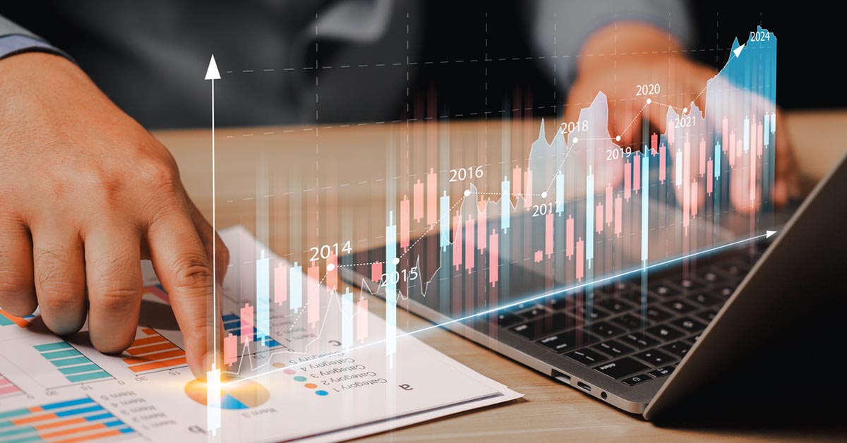 ノートパソコンと資料を使い、グラフやチャートの財務データを分析しているビジネスパーソンの手元