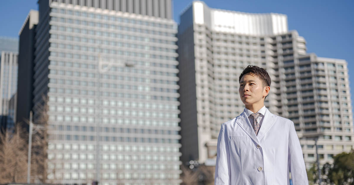 製薬会社を背景に立つ薬事職の男性の写真