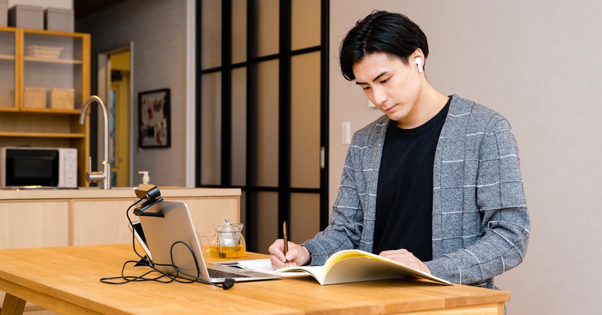 自宅でリスキリングの学習をする男性がノートPCと教材を使って勉強している様子