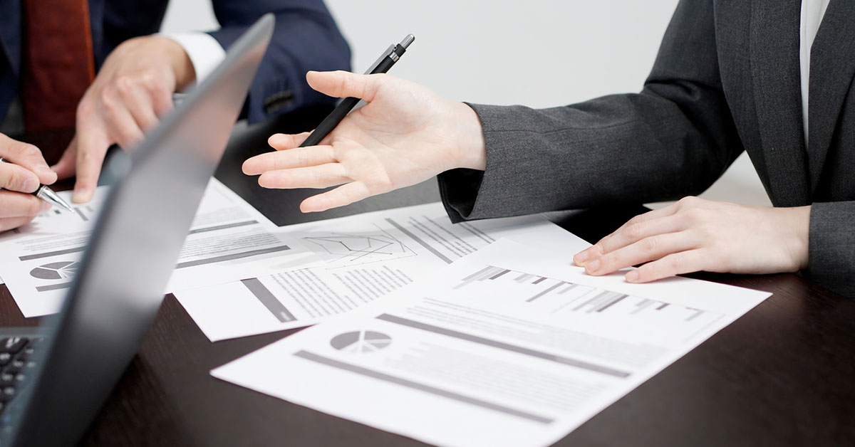 書類とパソコンのデータを確認しながら議論する会社員の手元