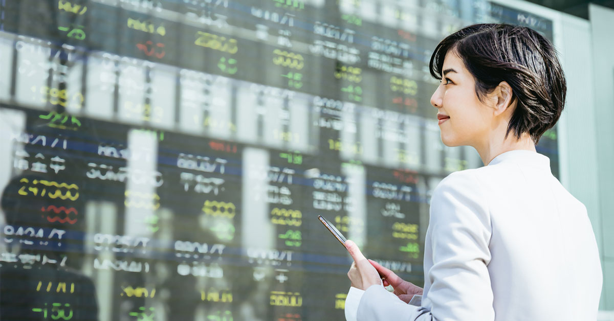 40代の転職に役立つ金融資格を取得し、株式市場ボードの前に立つ女性の図