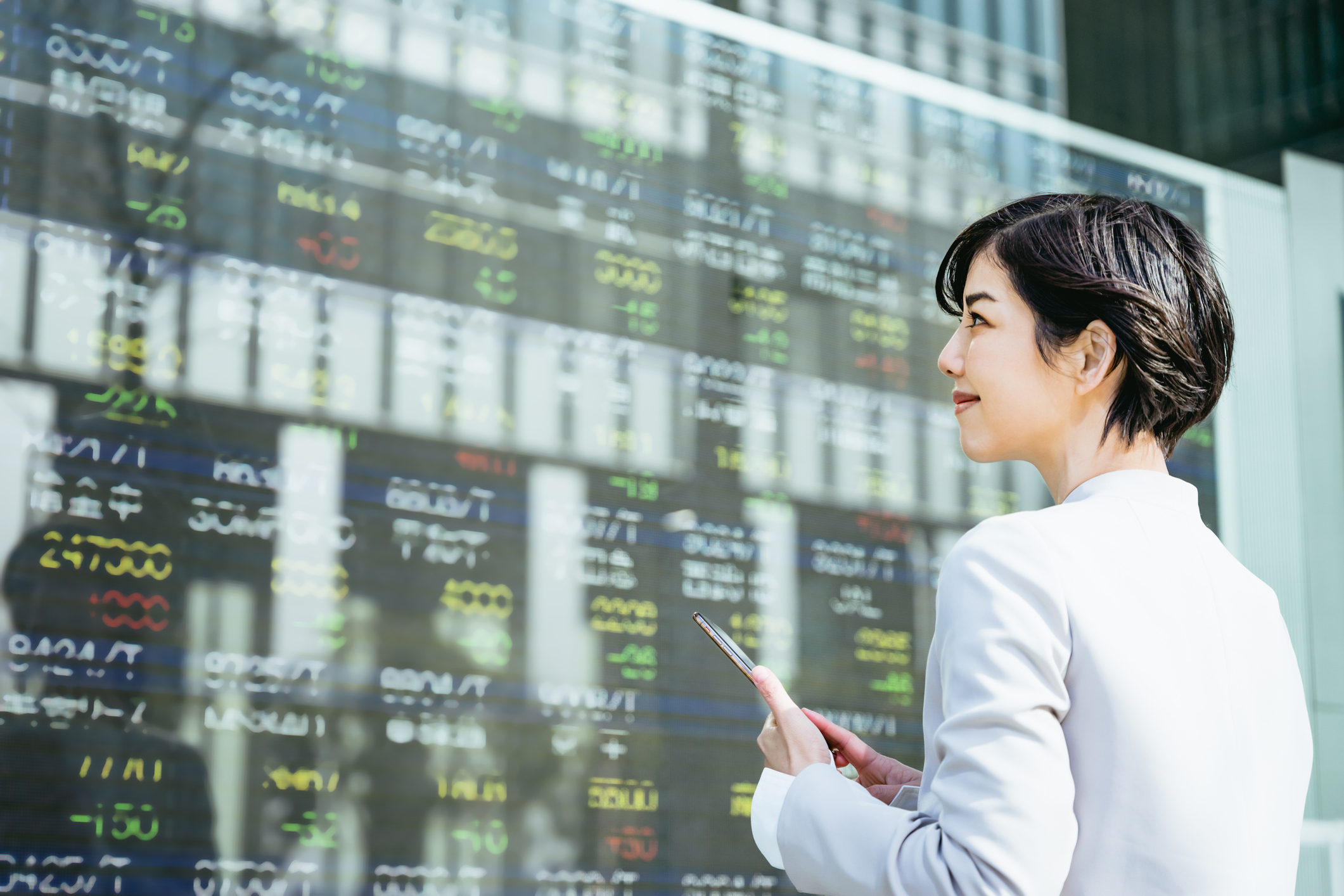 40代の転職に役立つ金融資格を取得し、株式市場ボードの前に立つ女性の図