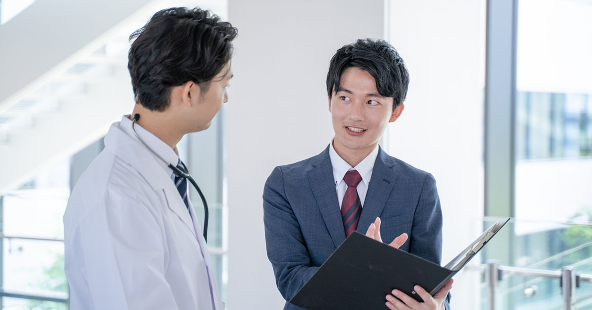 病院で医師とディスカッションする製薬会社のPMS担当者