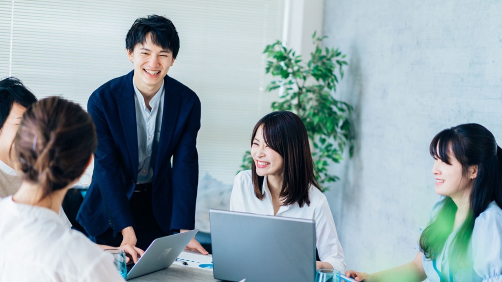 スタートアップ企業のオフィスで男女メンバーが会議テーブルを囲み、資料を確認しながら楽しそうに話し合う様子